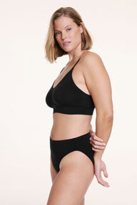 On a white studio backdrop, Sonnie wears the Cloud Cotton Triangle Bralette in Black in a side view, highlighting the soft stretch fabric, thin straps, and flexible underband.