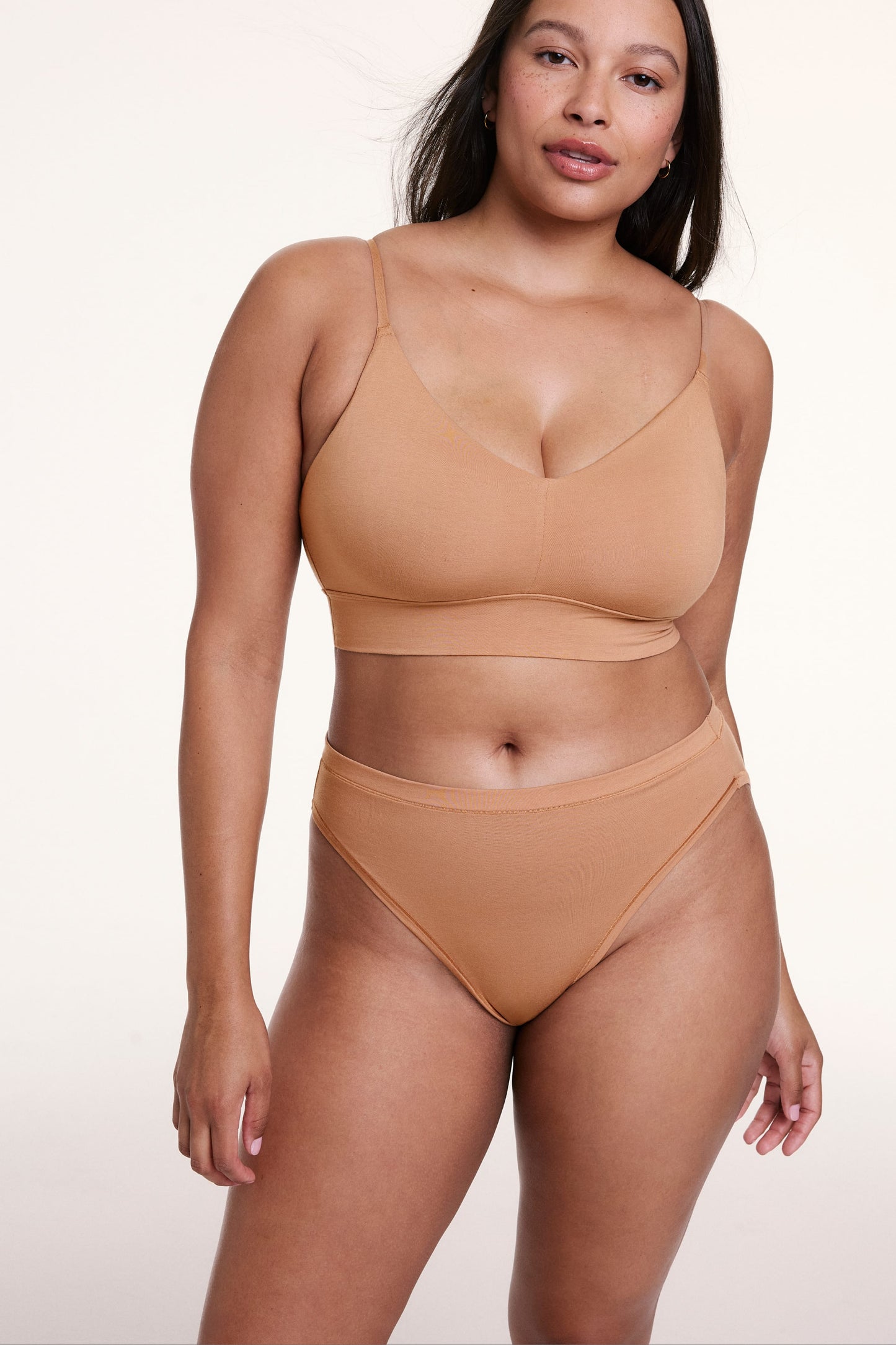 On a white studio backdrop, Alana wears the Cloud Cotton French Cut Brief in Dune with a matching bralette, standing front-facing to show the high-rise fit and soft cotton modal fabric.
