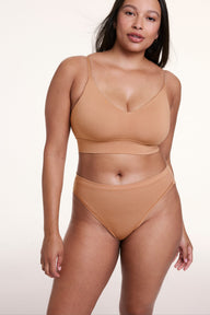 On a white studio backdrop, Alana wears the Cloud Cotton French Cut Brief in Dune with a matching bralette, standing front-facing to show the high-rise fit and soft cotton modal fabric.