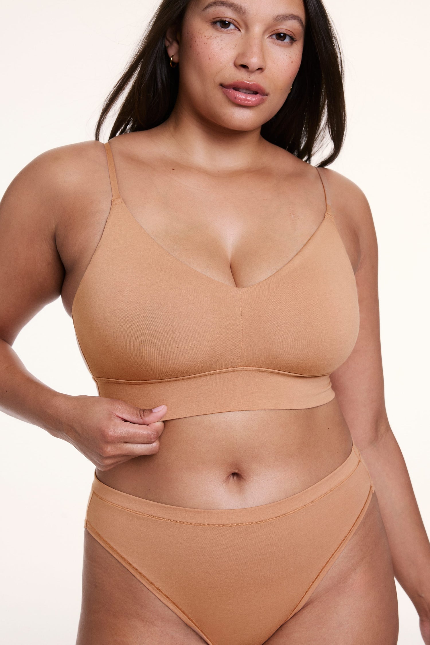 On a white studio backdrop, Alana wears the Cloud Cotton Triangle Bralette in Dune, shown close-up with a V neckline, thin adjustable straps, and a smooth underband. sizing: Alana wears size Large