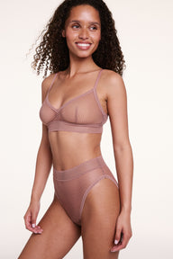 In a studio with a light neutral backdrop, Courtney wears the Dot Lace Triangle Bralette and Dot Lace French Cut Brief in Plum, featuring sheer dot lace fabric, adjustable straps, and a soft stretch lace band.