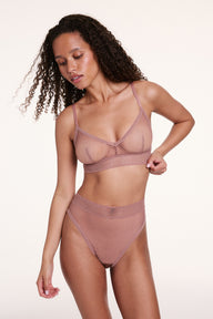 In a studio with a light neutral backdrop, Courtney wears the Dot Lace Triangle Bralette and Dot Lace French Cut Brief in Plum, highlighting the sheer dot lace fabric, V-neckline, and high-waist French cut brief with soft stretch lace waistband.