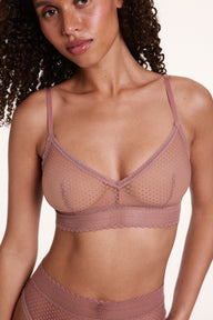 On a neutral studio backdrop, Courtney wears the Dot Lace Triangle Bralette in Plum with matching dot lace underwear, showing the sheer dot lace fabric, V-neckline, and thin adjustable straps. sizing: Courtney wears size Small