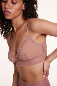 On a neutral studio backdrop, Courtney wears the Dot Lace Triangle Bralette in Plum in a side close-up view, highlighting the sheer dot lace fabric, V-neckline, and thin adjustable straps.