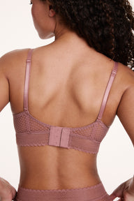On a neutral studio backdrop, Courtney wears the Dot Lace Triangle Bralette in Plum from the back, showing the adjustable straps, sheer dot lace band, and hook-and-eye back closure.