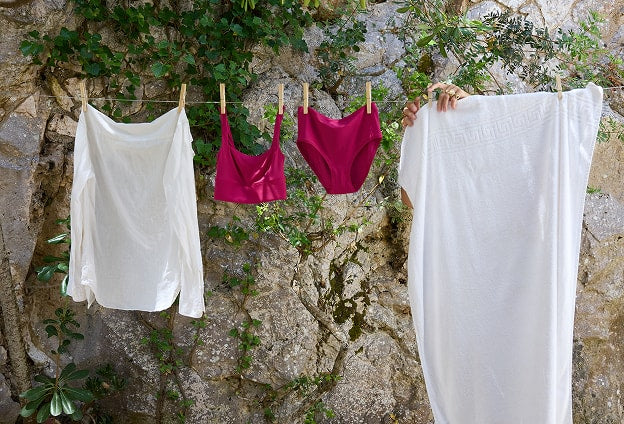 The Bliss Square Neck Bralette in Winterberry hanging on an outdoor clothesline among white linens against a stone wall.