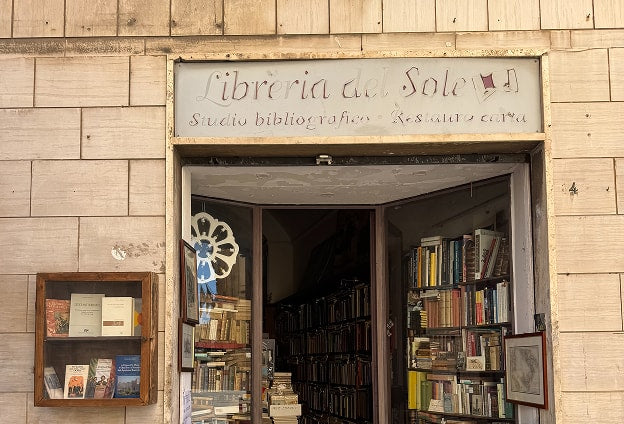 The exterior of Libreria del Sole, a sun-lit Italian bookshop with stacks of books spilling onto the street.