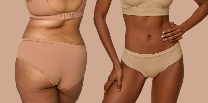 Two models standing side by side against a tan backdrop. The model on the left has her back to the camera wearing the Cloud Cotton Hiphugger in the color Dune. The model on the right is wearing the Bliss Hiphugger in Beige.