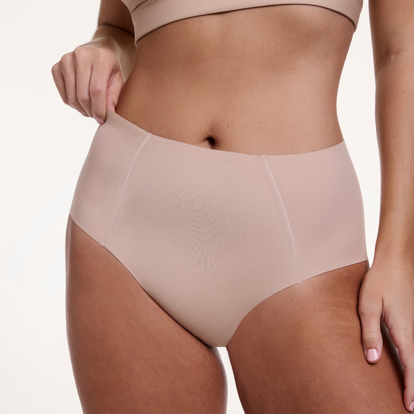On a white studio backdrop, Sonnie wears the No-Show Highwaist Brief in Beige, highlighting the high-waisted silhouette and soft, no-show fabric for a smooth, second-skin feel.