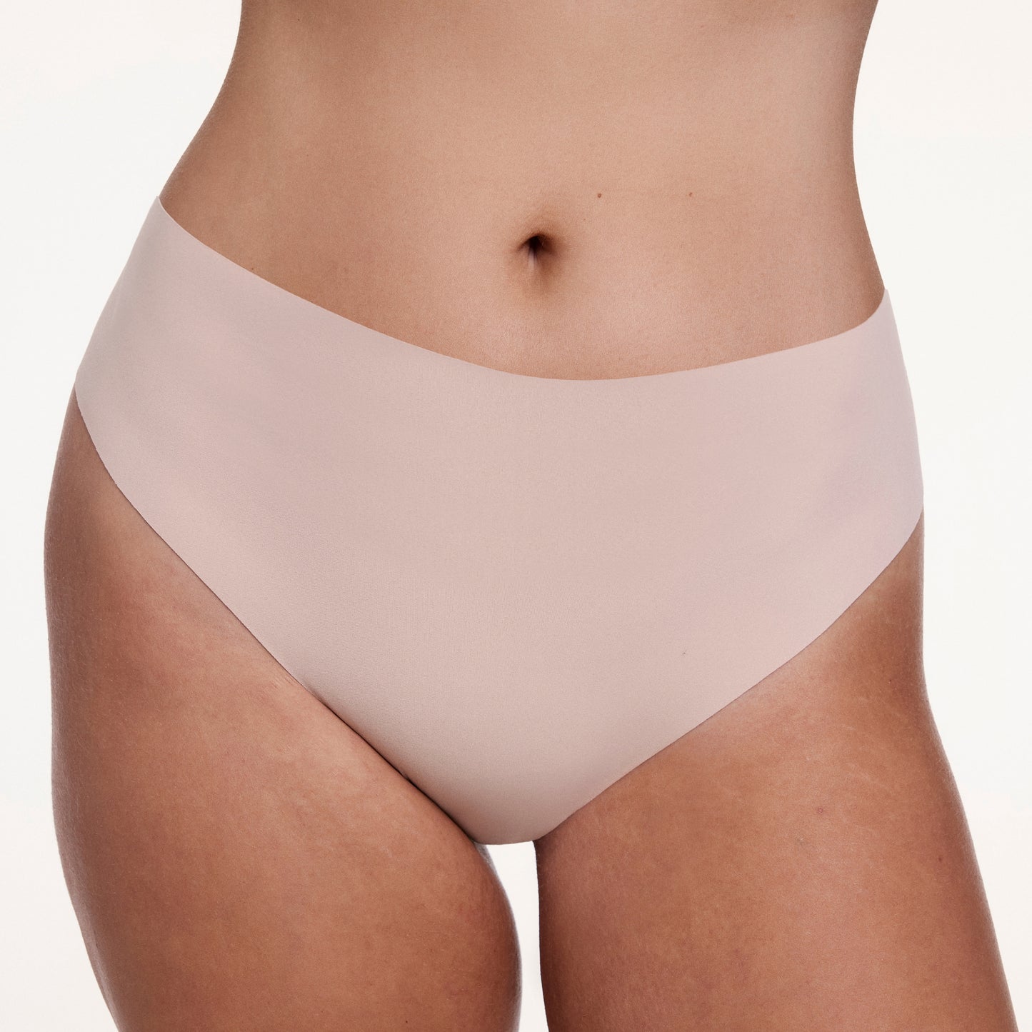 On a white studio backdrop, Sonnie wears the No-Show Highwaist Thong in Beige, highlighting the high-waisted silhouette and soft, no-show fabric that creates a smooth, second-skin look.