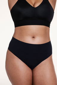 On a white studio backdrop, Alana wears the No-Show High Waist Thong in Black, shown from the front with a high-rise fit and smooth, no-show fabric. sizing: Alana wears size Large