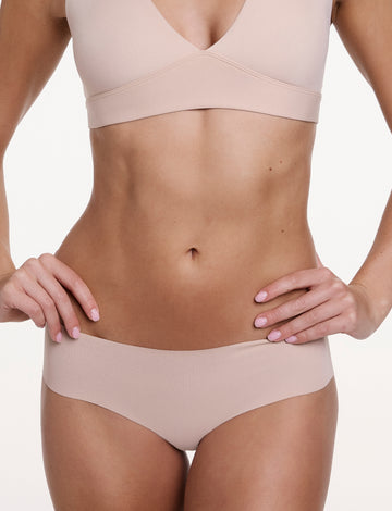 On a white studio backdrop, Gianna wears the No-Show Hiphugger in Beige, shown from the front with a mid-rise fit, wide waistband, and smooth, no-show finish. sizing: Gianna wears size Small
