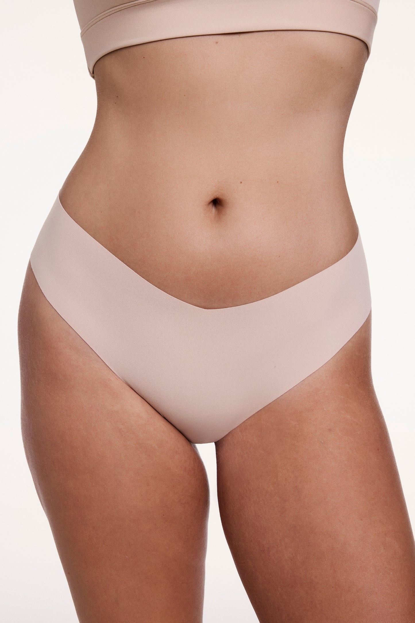On a white studio backdrop, Sonnie wears the No-Show Low Rise Thong in Beige, shown from the front with a low-rise waistband and raw-edge finish designed to sit flat against the skin. sizing: Sonnie wears size Large