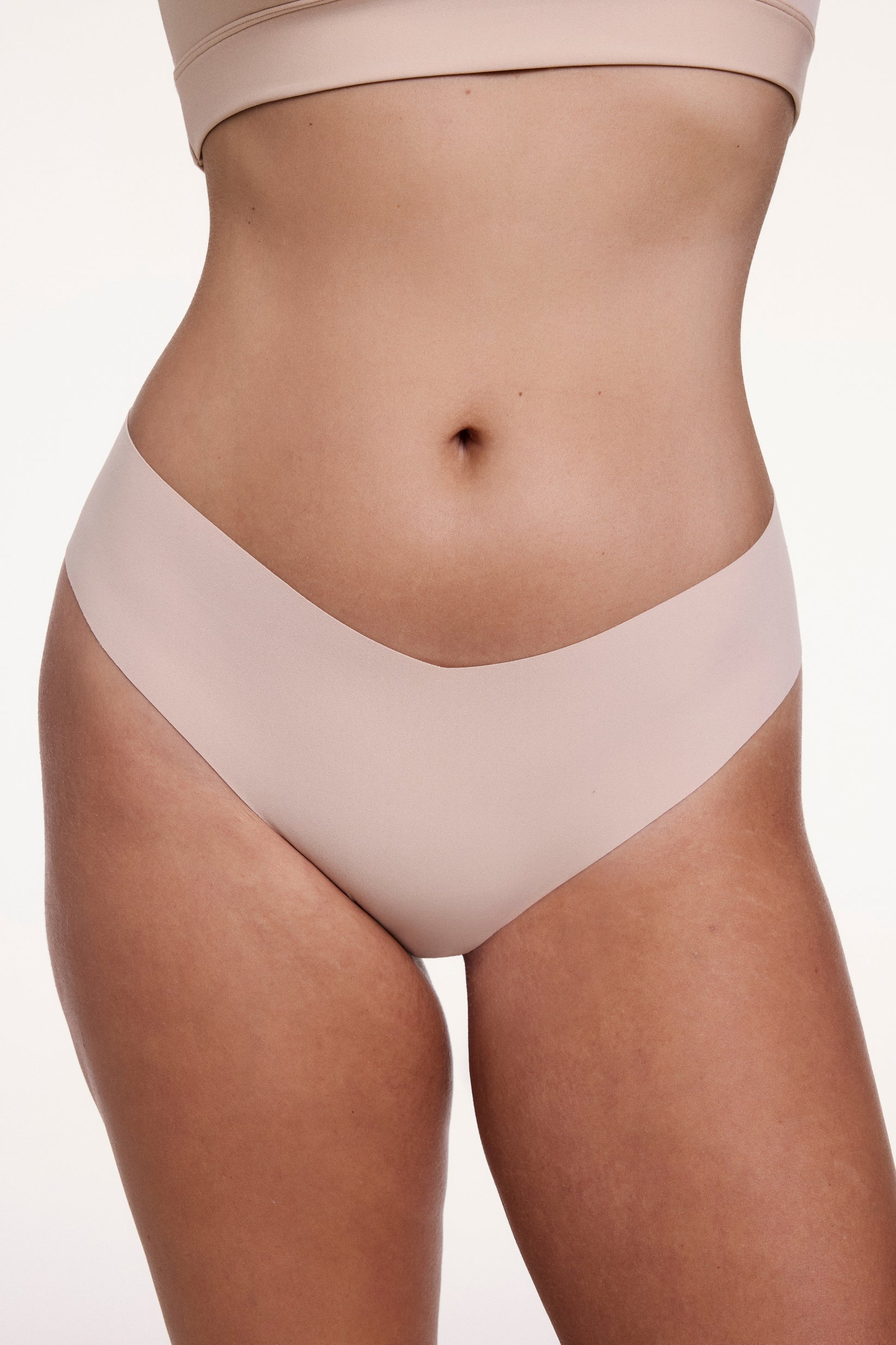 On a white studio backdrop, Sonnie wears the No-Show Low Rise Thong in Beige, shown from the front with a low-rise waistband and raw-edge finish designed to sit flat against the skin. sizing: Sonnie wears size Large