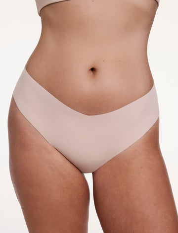 On a white studio backdrop, Sonnie wears the No-Show Low Rise Thong in Beige, shown from the front with a low-rise waistband and raw-edge finish designed to sit flat against the skin. sizing: Sonnie wears size Large