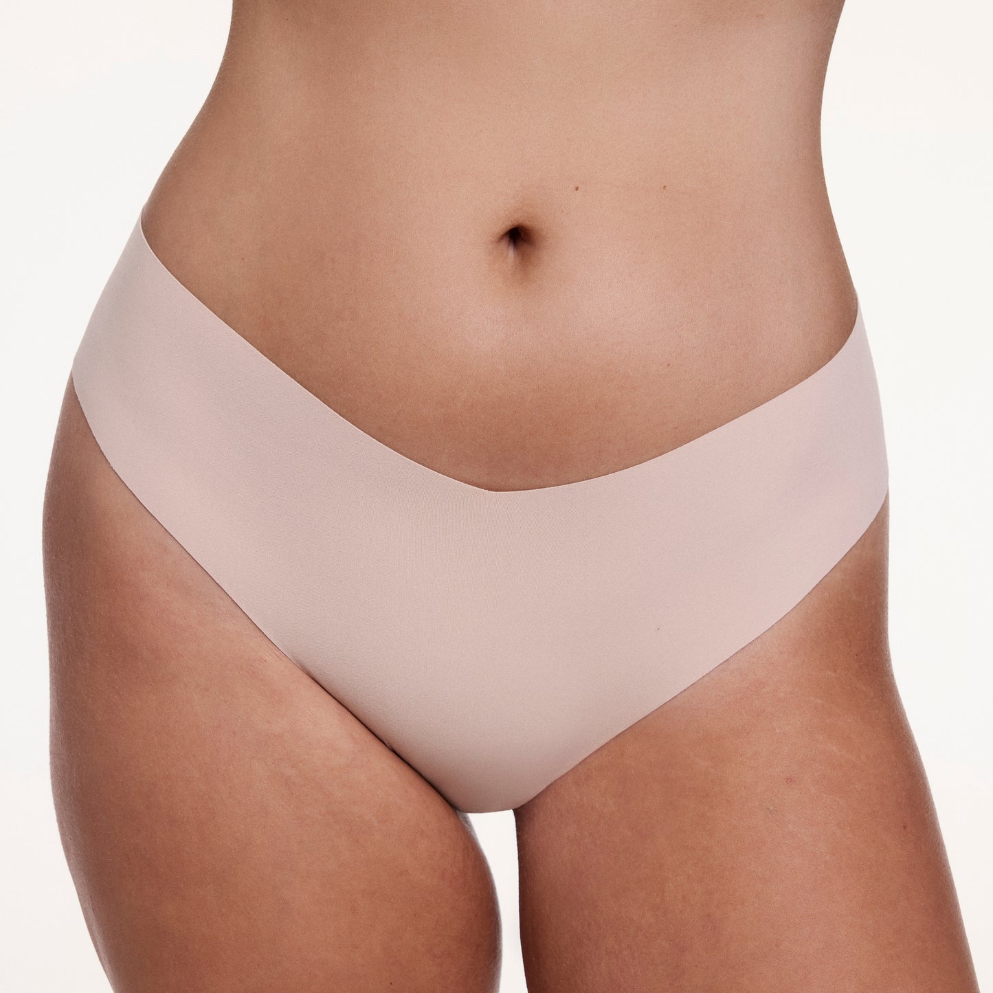 On a white studio backdrop, Sonnie wears the No-Show Low Rise Thong in Beige, highlighting the low-rise silhouette and soft, no-show fabric for a smooth, second-skin feel.