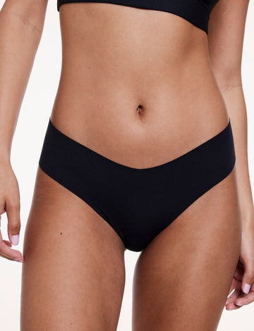 On a white studio backdrop, Courtney wears the No-Show Low Rise Thong in Black, shown from the front with a low-rise fit and smooth, no-show fabric. sizing: Courtney wears size Small