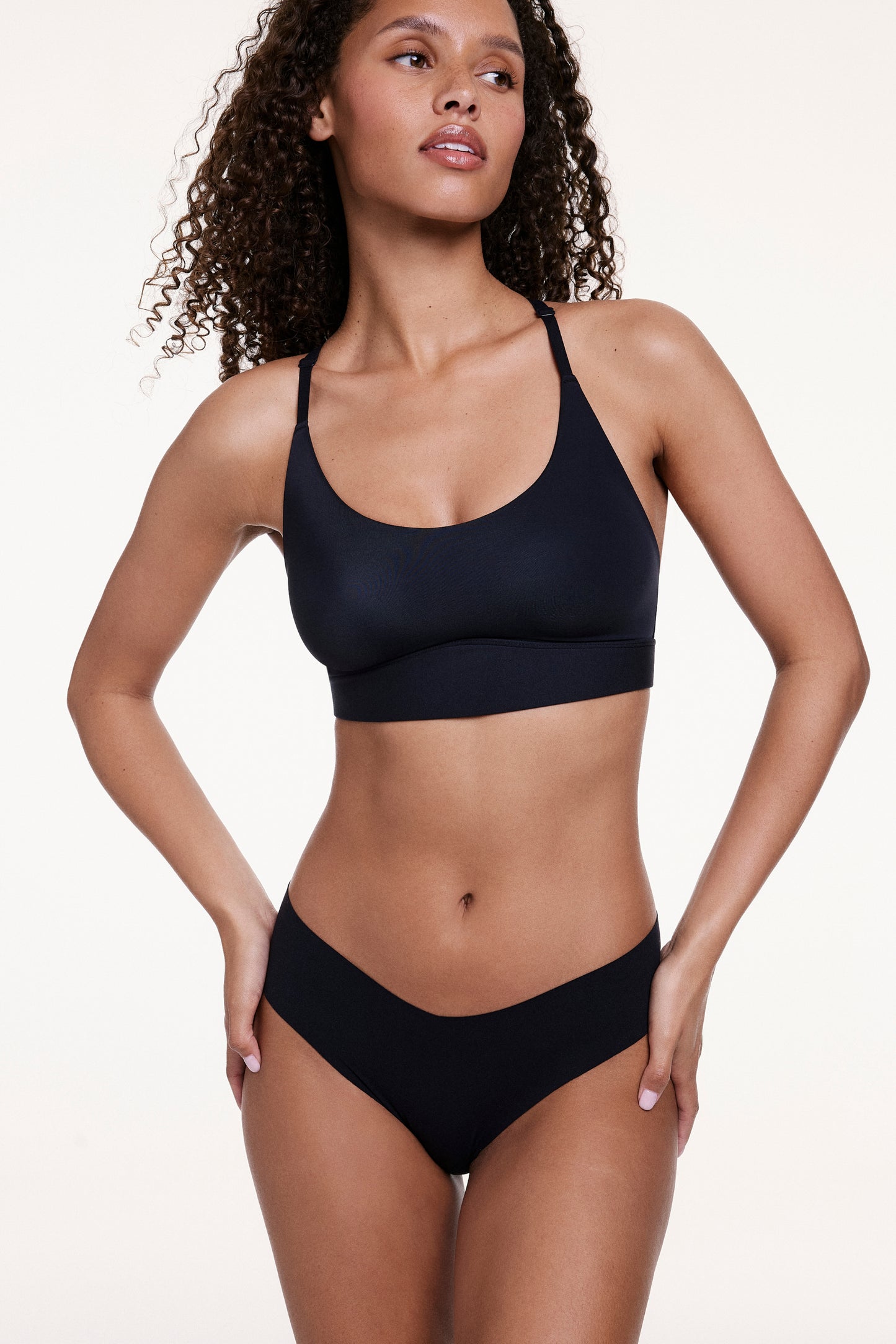 “Full-body view of Courtney wearing the No-Show Low Rise Thong in Black with a matching bra, highlighting the low-rise fit and smooth, no-show finish.