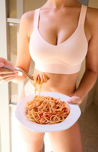 Close-up torso of BlissSmooth Bralette in Rose, model holding a plate of spaghetti