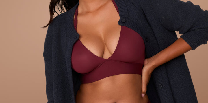 A model wears the Bliss Lace Halterneck Bralette and matching Bliss Lace Highwaist Brief in Bordeaux. She’s styled with an open navy cardigan, showcasing the bralette’s deep V and smoothing band.