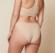 Carli is shown from the back wearing the Bliss Racerback Bralette and the Bliss Bikini in Beige, displaying the back view of the set.