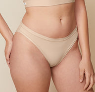 A close-up side view of Carli, focusing on her lower body. She is wearing the Bliss Bikini in Beige, showcasing the design and fit of the underwear. 