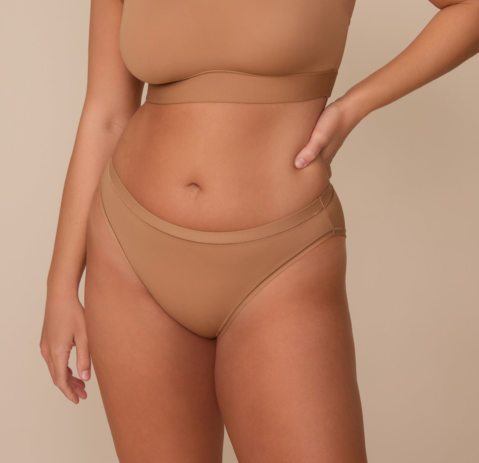 Sonnie wearing the Bliss Bikini in Tan. The mid rise waistband and comfortable seams are emphasized. sizing; Sonnie wears size Large