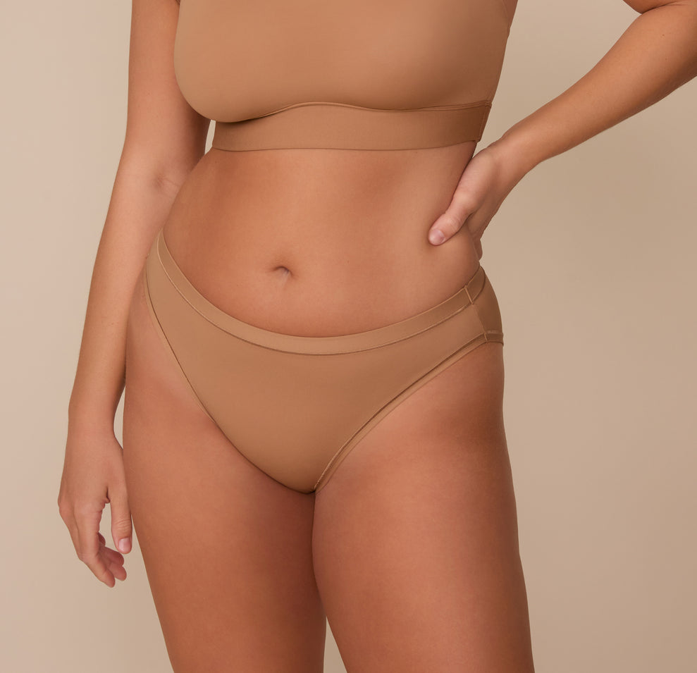 Sonnie wearing the Bliss Bikini in Tan. The mid rise waistband and comfortable seams are emphasized. sizing; Sonnie wears size Large