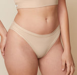 A close-up side view of Carli, focusing on her lower body. She is wearing the Bliss Bikini in Beige, showcasing the design and fit of the underwear.