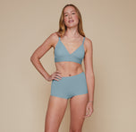 Model standing with her right hand on her hip and her left arm down by her side. She’s wearing the Bliss Triangle Bralette and matching Bliss Boyshort in the color Mist.