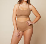 Model standing with her left hand on her hip and her right arm down by her side. She’s wearing the Bliss Racerback Bralette and matching Bliss Boyshort in the color Tan. sizing: Summerlyn wears size Large