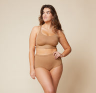 Model standing with her left hand on her hip and her right arm down by her side.  She’s wearing the Bliss Racerback Bralette and matching Bliss Boyshort in the color Tan.