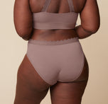 Back view of Akesha wearing the Bliss Lace Highwaist Brief and matching Bliss Lace Halterneck Bralette in Mauve. The image emphasizes the full-coverage design of the brief and the lace-back design of the bralette.
