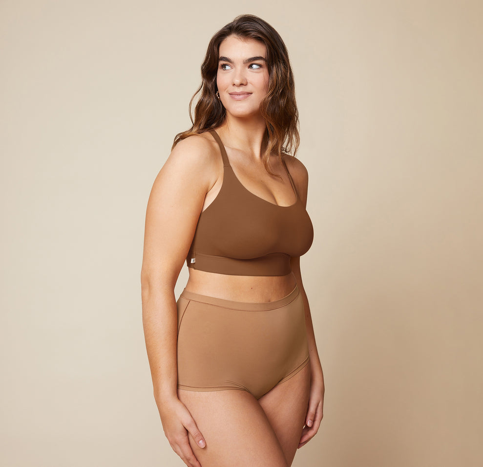 Summerlyn standing with her arms relaxed by her sides, wearing the Bliss Racerback Bralette in Brown and the Bliss Boyshort in Tan. The image shows the front view of the set, emphasizing the smooth fabric and secure fit. sizing: Summerlyn wears size Large