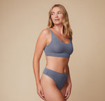 Side view of the model wearing the Cloud Cotton Scoop Bralette and matching bottom in Slate. She places one hand on her hip, highlighting the bralette’s scoop neckline of the bralette.