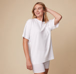 Model Megan in the Cloud Cotton Tee in White and Cloud Cotton Logo Boxer Brief in White, standing with one hand resting on her head. The lightweight and breathable fabric is emphasized.