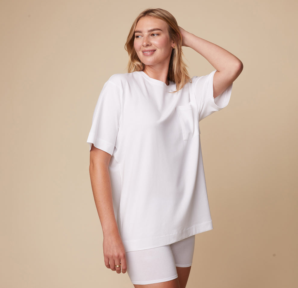 Model Megan in the Cloud Cotton Tee in White and Cloud Cotton Logo Boxer Brief in White, standing with one hand resting on her head. The lightweight and breathable fabric is emphasized.