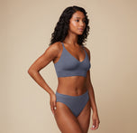 Model poses in a side view, wearing the Cloud Cotton Triangle Bralette and matching bottom in Slate. She places one hand on her hip, highlighting the bralette’s triangular shape and fit.