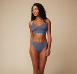 Full-body view of the model smiling confidently, modeling the Cloud Cotton Triangle Bralette and matching bottom in Slate. She stands with one hand resting lightly on her hip.