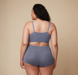 Back view of a second model wearing the Cloud Cotton Triangle Bralette and matching bottom in Slate. Her posture is relaxed as she stands against a simple backdrop. sizing: Bianca wears size 2XL
