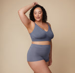 Model poses with one hand resting on her head while wearing the Cloud Cotton Triangle Bralette and matching bottom in Slate. The neutral backdrop keeps the focus on her pose and the fit of the set.