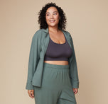 Model Bianca wearing the Pima PJ Longsleeve in Rainforest, left unbuttoned, revealing the Lounge Rib Scoop Bralette in Charcoal underneath. The casual, comfortable fit of the PJ set is emphasized.