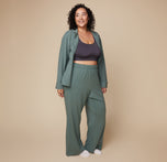 Model Bianca wearing the Pima PJ Pants in Rainforest paired with the Lounge Rib Scoop Bralette in Charcoal and an open Pima Long sleeve. The soft, wide-leg pants offer a relaxed and comfortable fit.