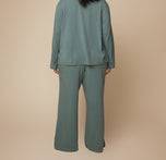 Back view of model Bianca wearing the Pima PJ Pants in Rainforest paired with the Pima Longsleeve. The loose, flowy fabric of the wide-leg pants is showcased from behind.