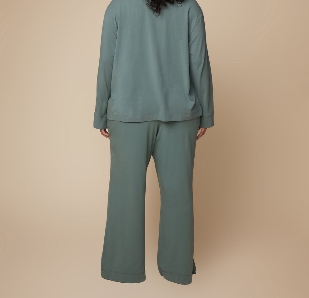 Back view of model Bianca wearing the Pima PJ Pants in Rainforest paired with the Pima Longsleeve. The loose, flowy fabric of the wide-leg pants is showcased from behind.