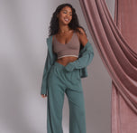 Model Ally wearing the Pima PJ Longsleeve in Rainforest, left open to reveal the Lounge Rib Triangle Bralette in Oyster. The relaxed pose emphasizes comfort and softness, highlighting the casual loungewear look.