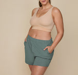 Model Summerlyn wearing the Pima PJ Shorts in Rainforest (Size: L) paired with the Base Bralette in Beige. The image emphasizes the elastic waistband and comfortable, casual style of the shorts.