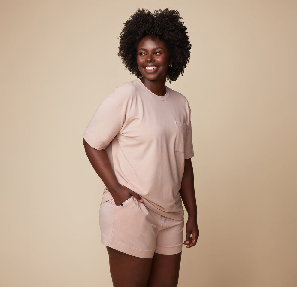Model Akesha standing in the Pima Tee in Bellini with Pima PJ Shorts, smiling in a relaxed pose. The lightweight and breathable fabric emphasizes comfort.