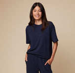 Model Anna wearing the Pima Tee in Navy paired with Pima PJ Pants, standing with hands in pockets. The relaxed, comfortable fit and soft fabric are highlighted.
