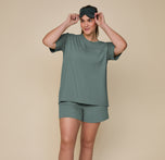 Model Summerlyn standing in the Pima Tee in Rainforest and Pima PJ Shorts, with a sleep mask on her head. The relaxed, comfortable fit is showcased in this full-length shot.